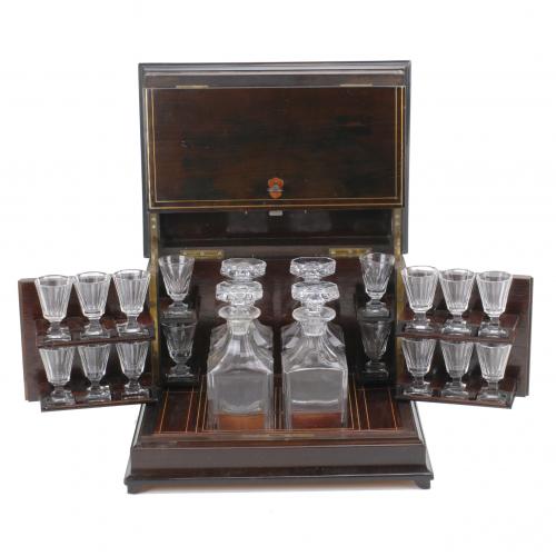 En madera de palisandro con marquetería en latón dorado, con laterales abatibles.Incluye cuatro licoreras y dieciséis copas de cristal.Con llave.25 x 35 x 24.5 cms. caja,19.5 cms. alt. licoreras y7 cms. alt. copas.